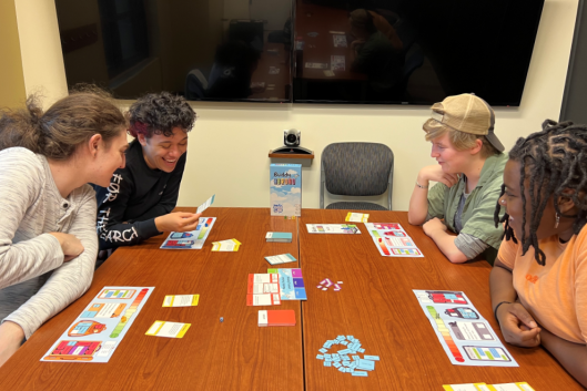 Four students play a board game on a brown table