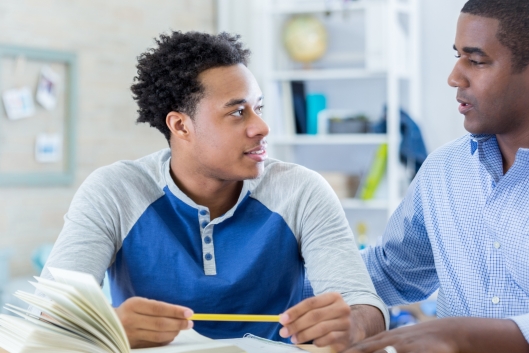 Black male student listens attentively to older adult giving guidance.