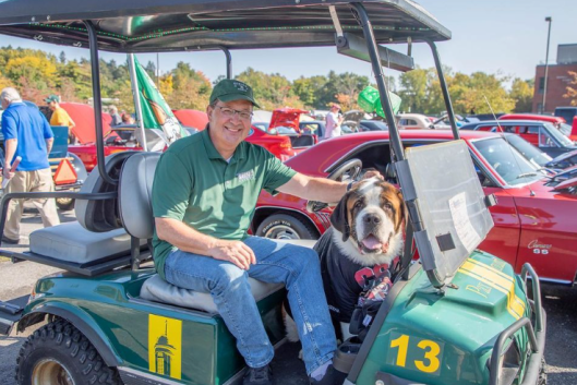 President Chuck Seifert sits in a green golf cart with school mascot, Baloo.