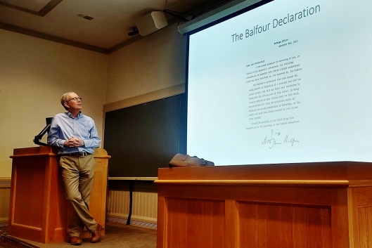 Derek Penslar leans on a podium, looking up at a projected slide about the Balfour Declaration.