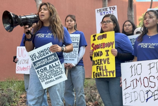 A group of undocumented students hold protest signs. One yells into a bullhorn.