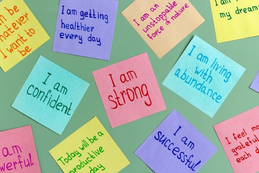 A green background decorated with colorful sticky notes featuring affirmations such as "I am confident" "I am strong" "I am living with abundance"