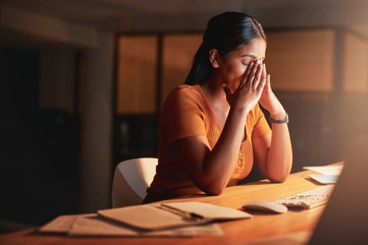 Woman at her desk with her hands on her face looking burned out and stressed.