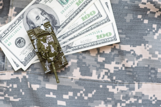Money on top of a military uniform with a toy tank on both