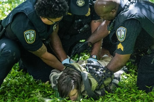 A person held face-down in the grass by several police officers.