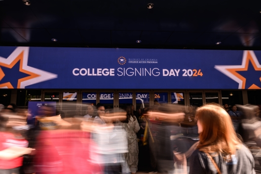 People moving in front of a sign that says College Signing Day 