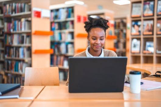 Young adult Hispanic female sitting at a desk in a library working on a computer