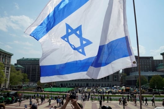 An Israeli flag waves in the foreground in a photo of Columbia University’s campus.