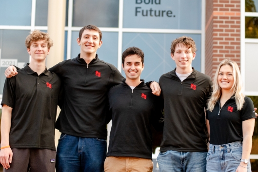 A group of Gonzaga students smile for a photo wearing matching black polos with a Gonzaga Sport Consulting Group logo