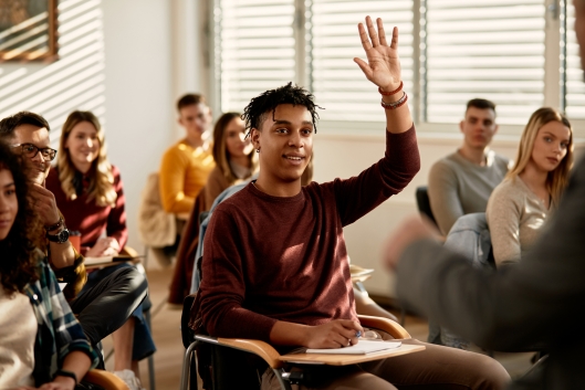 Smiling African American student raising his hand to ask a questing during a class at lecture hall.