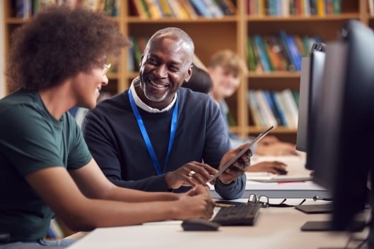 A male staff member helps a young male student on a library computer
