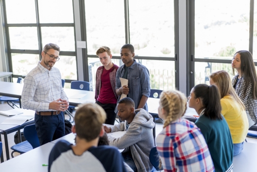 Multiethnic students and male teacher are discussing at school. They are casually dressed.
