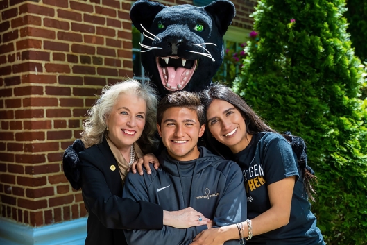 Three people pose for a photo with a panther mascot above them