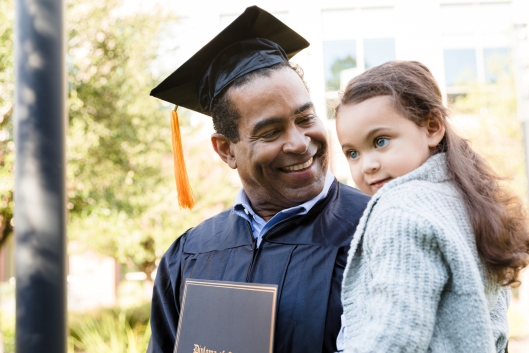 After his graduation ceremony, a man carries a preschool-age child in his arms.