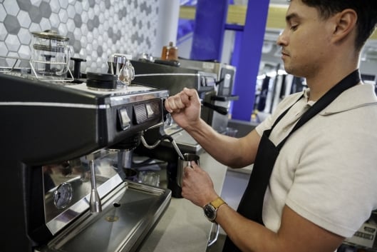 Young Hispanic man in his 20s frothing and steaming milk at a commercial espresso machine 