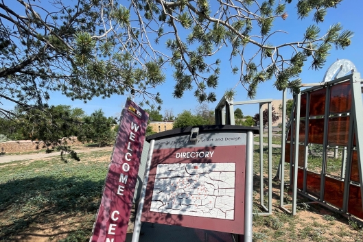 A maroon welcome sign and a campus directory with a map are heavily leaning, as in disrepair.
