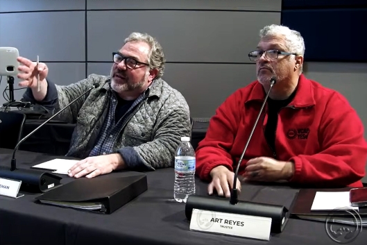 Mott Community College board members Michael Freeman and Art Reyes sit behind a desk, gesticulating, at a November board meeting. 