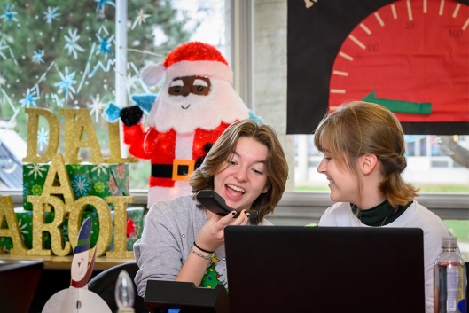 Two students answer the phone singing in a Christmas-decorated room