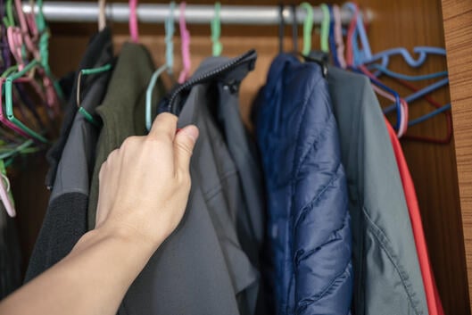 Hand choosing winter jacket on clothes rack in wood closet