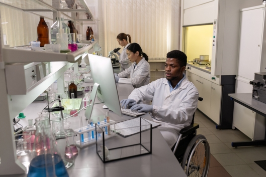 Three young researchers work in a science lab; the researcher in the foreground uses a wheelchair.
