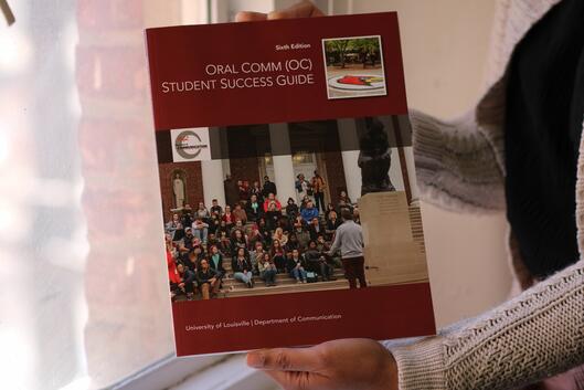 An unidentified person holds a printed version of the University of Louisville Oral Comm Success Guide