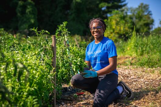 A student wearing a blue shirt poses in a garden. 