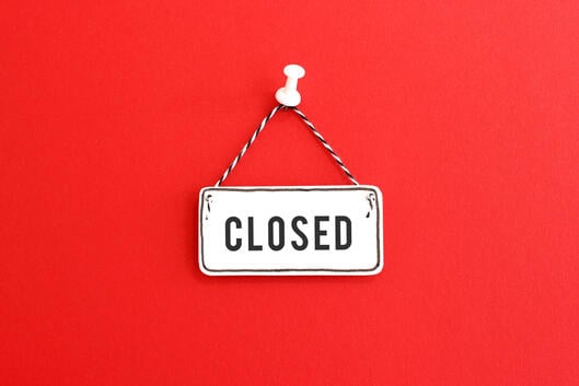 A photo of a handmade "closed" sign, on clapboard, tacked to a red background.