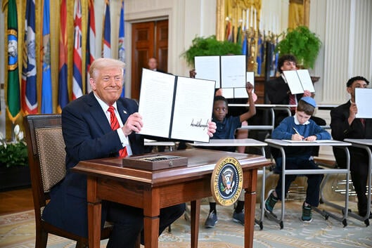 President Donald Trump holds up a signed executive order to dismantle the Department of Education. 