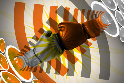 Photo illustration: Two boxing gloves collide with each other. Next to each glove is a speaker showing audio lines coming from them.