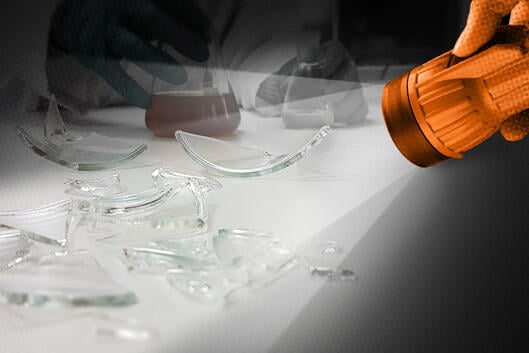A flashlight shines a light on broken glass lab equipment. 