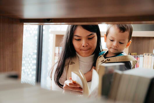 Young mother reading books to little son in library.