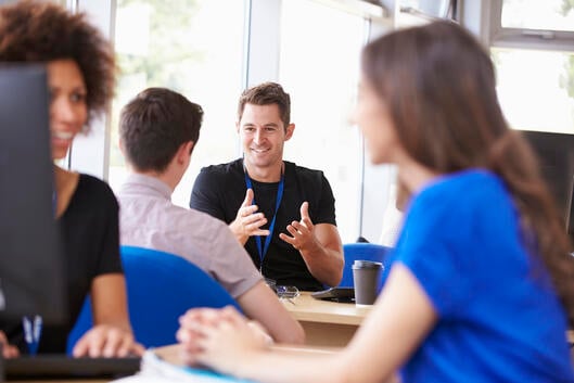 A counselor is speaking to a male student. Two women are in the foreground but are not the subject of the photo.