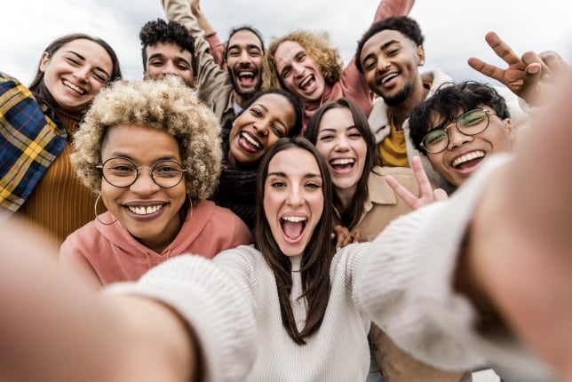 A diverse group of college students gather together, smiling, and take a selfie (photo is taken from selfie angle).