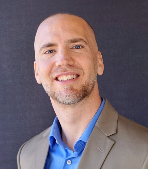 A head shot of Matthew Garrett, history professor at Bakersfield College, in a blue shirt and tan jacket on a navy blue background.