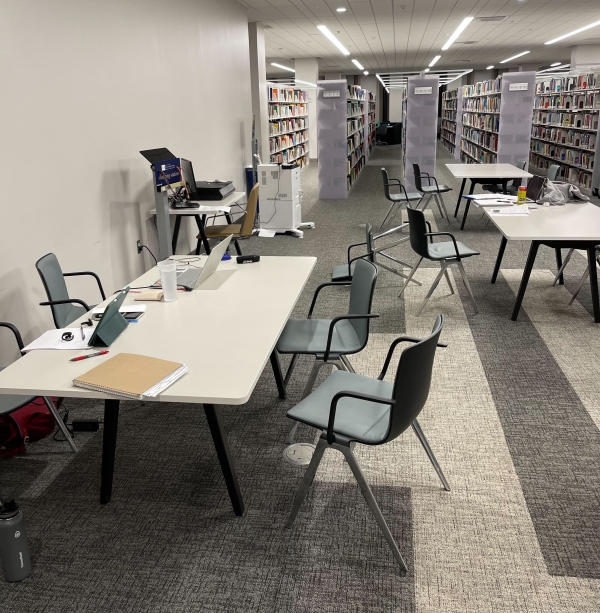 An empty library with chairs askew and lots of notebooks and digital devices left behind.