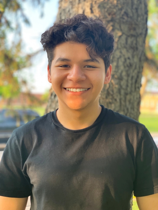 A Latino man wearing a black shirt stands in front of a tree outside.