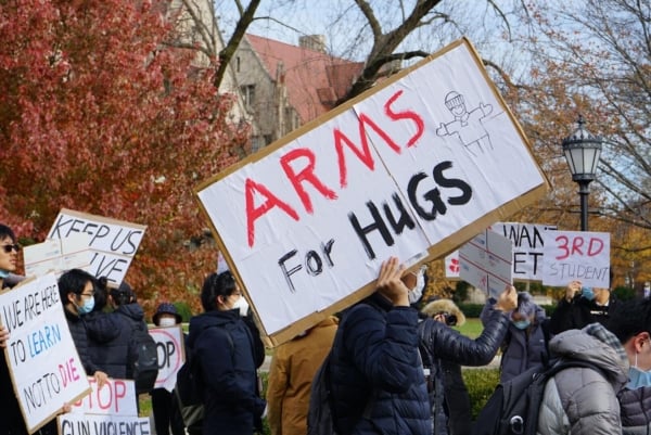 A man in a face mask holds a sign reading "Arms for Hugs" among other people holding signs