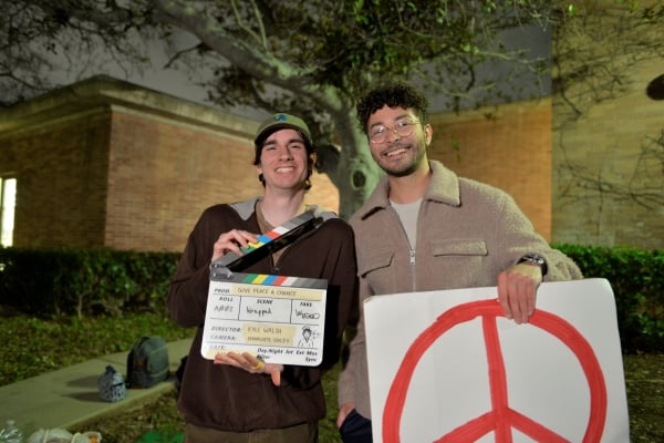 Two students hold signs, one is a film clapper