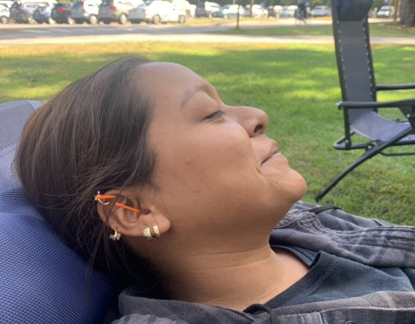 A student lies on a chair with two orange acupuncture needles in her ear.