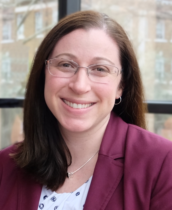 Calley Stevens Taylor, a light-skinned woman with brown hair and glasses, smiles for a headshot