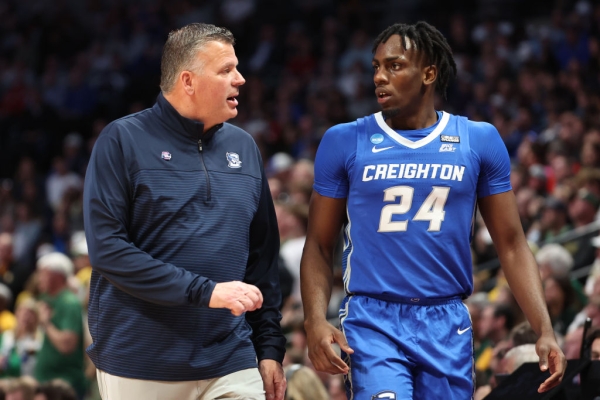 A white coach and a Black basketball player walk side by side on the court.