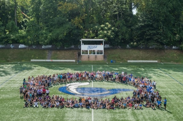 Students gathered around the Cabrini logo on an athletics field.