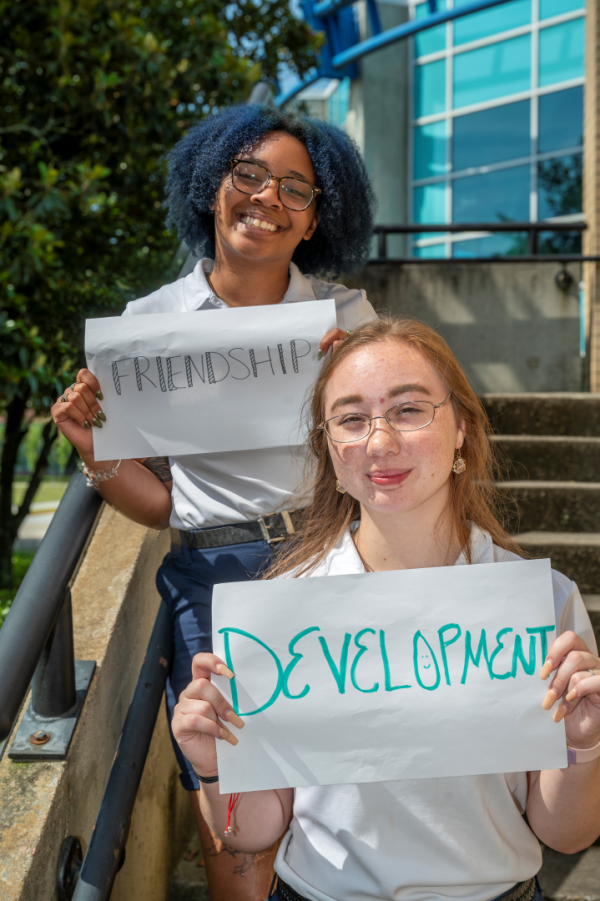 Two students hold white paper signs with the words friendship and development written on them.