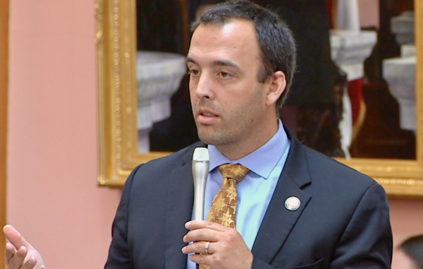 A man in a suit and tie speaks into a microphone.