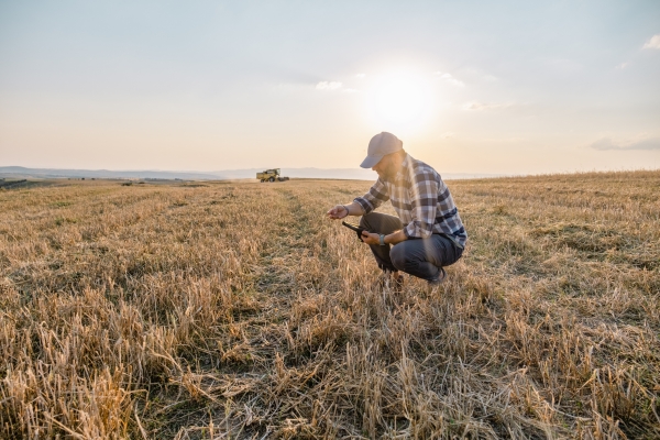 A man holding a digital tablet squats in a field