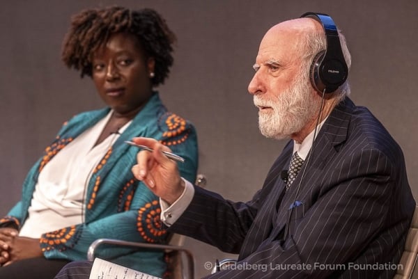 A Black woman and an older white man wearing headphones engage in a conversation.