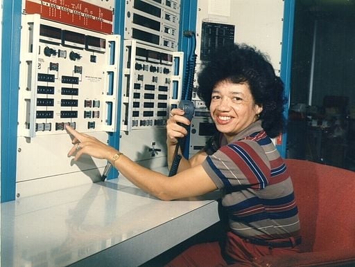 A photo of a smiling woman with light-brown skin and dark hair in front of a dated computer.