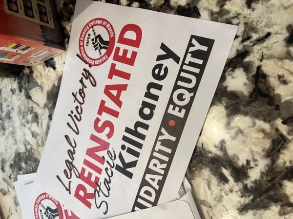 A sign on the floor reads, "Legal Victory! REINSTATED Stacie Kilhaney," in red and black letters.