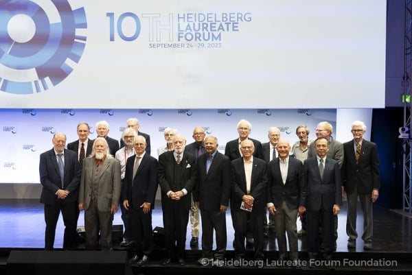 A group of older, well-dressed men standing in front of a sign that says, "10th Heidelberg Laureate Forum."