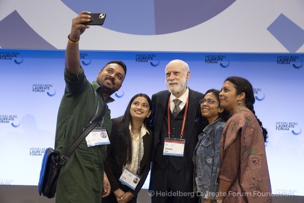 An older man in a suit poses for a selfie with four young researchers.